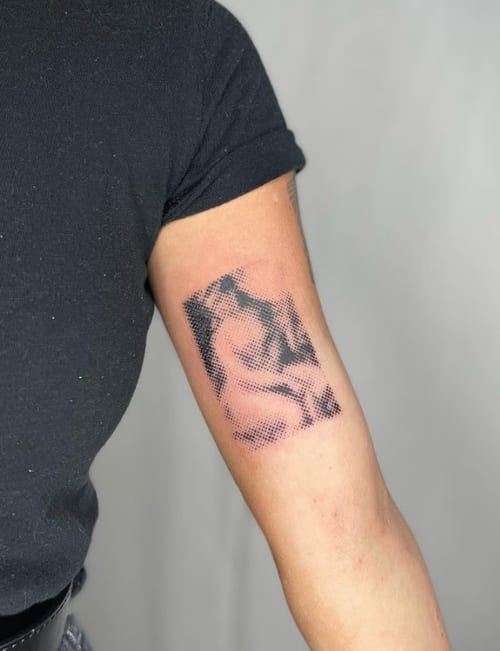 A black and grey dotwork tattoo of a woman on the upper arm, featuring intricate shading and a pixelated effect — by Level tattoo, los angeles