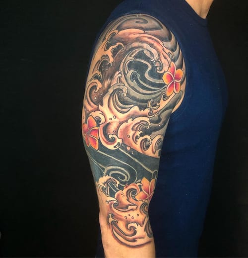 A bold Japanese-style tattoo featuring ocean waves and flowers in color on the upper arm — by Sandra Price, los angeles