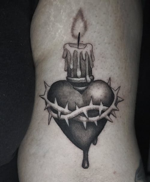 A black and grey tattoo of a heart with a candle on top and thorns wrapped around it, located on the arm — by Miguel ANGELO, los angeles