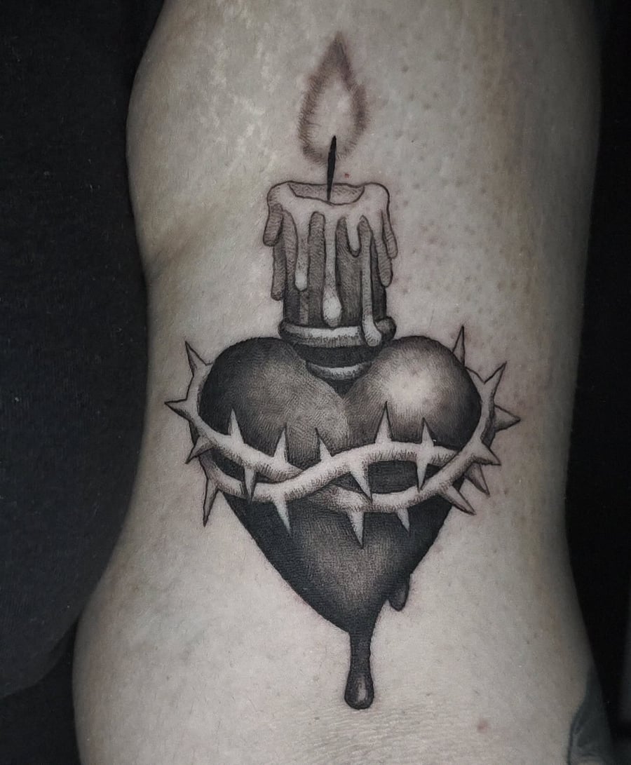 A black and grey tattoo of a heart with a candle on top and thorns wrapped around it, located on the arm — by Miguel ANGELO, los angeles