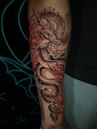A Japanese-style dragon tattoo on the forearm, featuring intricate black and grey shading with red accents for flames — by Josue Bravo, los angeles