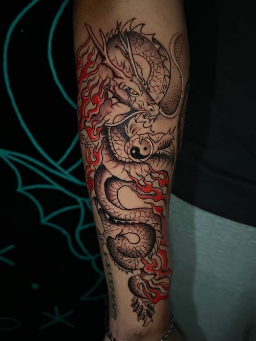 A Japanese-style dragon tattoo on the forearm, featuring intricate black and grey shading with red accents for flames — by Josue Bravo, los angeles