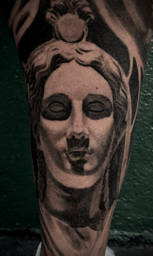 A black and grey realism portrait of a serene face on the leg, featuring detailed shading and soft contrasts — by tyler_whitlock, los angeles