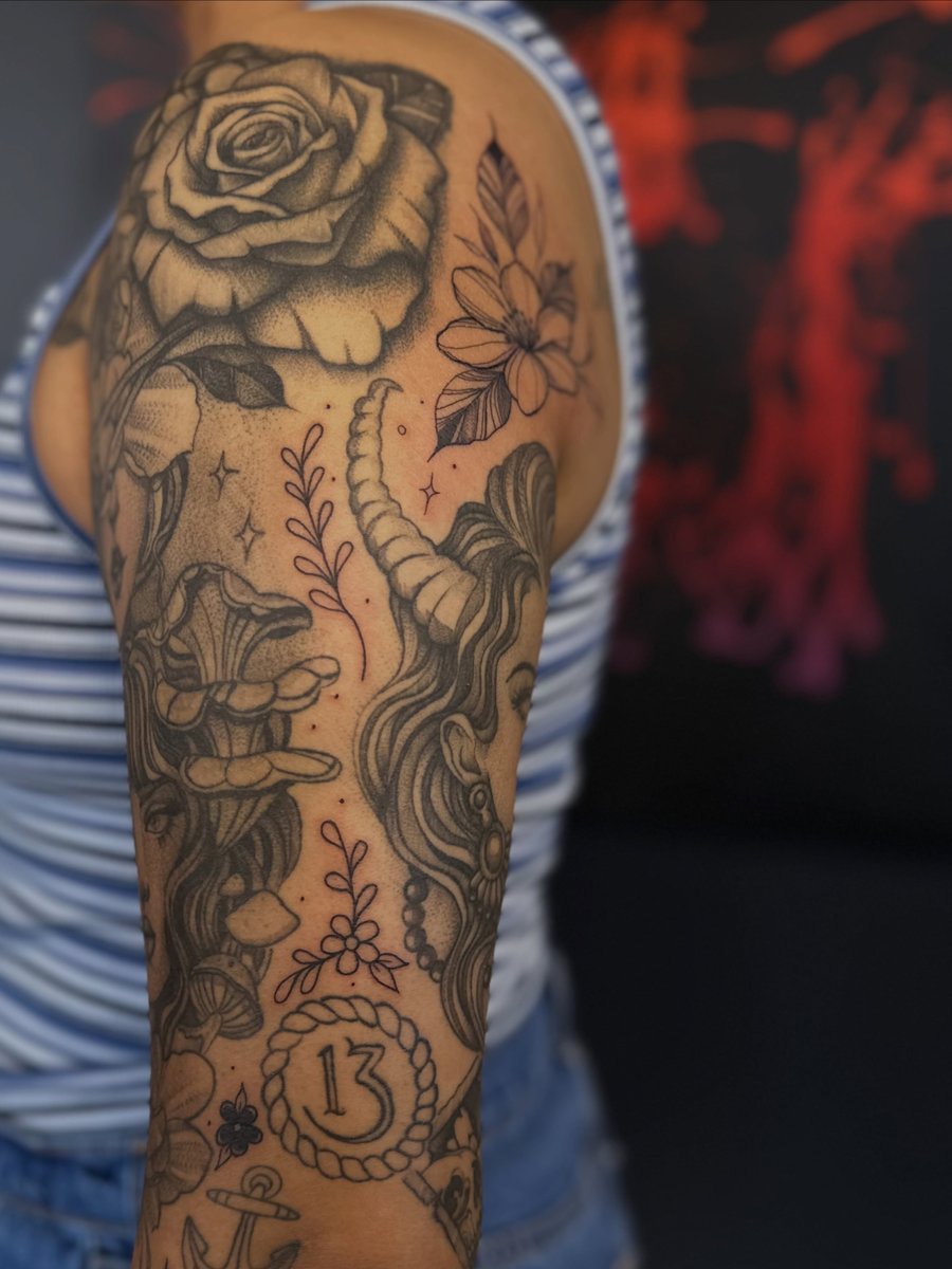 A black and grey tattoo of a woman with horns and flowers on the upper arm in an illustrative style — by Maddie Ramirez, los angeles