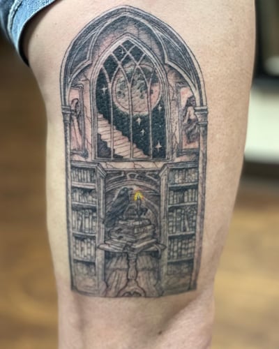 A detailed black and grey tattoo of a gothic library with a raven, moon, and candle on the thigh — by Sandra Price, los angeles