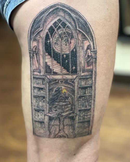 A detailed black and grey tattoo of a gothic library with a raven, moon, and candle on the thigh — by Sandra Price, los angeles