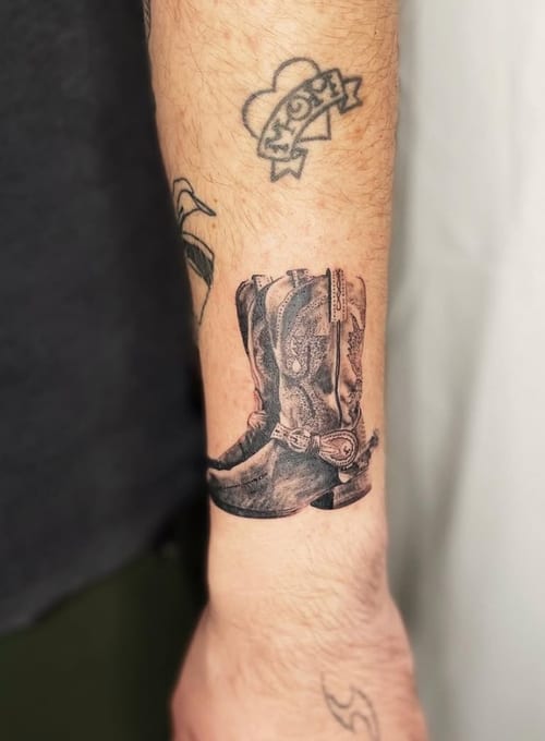 A black and grey realism tattoo of a cowboy boot on the forearm with detailed shading and texture — by Level tattoo, los angeles