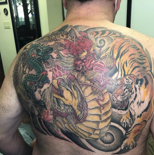 A bold and colorful Japanese style tattoo featuring a dragon and tiger on the back, showcasing intricate details and vibrant colors — by Sandra Price, los angeles