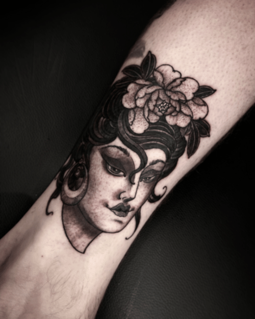 A black and grey neo-traditional tattoo of a woman's face with a flower in her hair on the leg, featuring bold lines and shading — by tyler_whitlock, los angeles