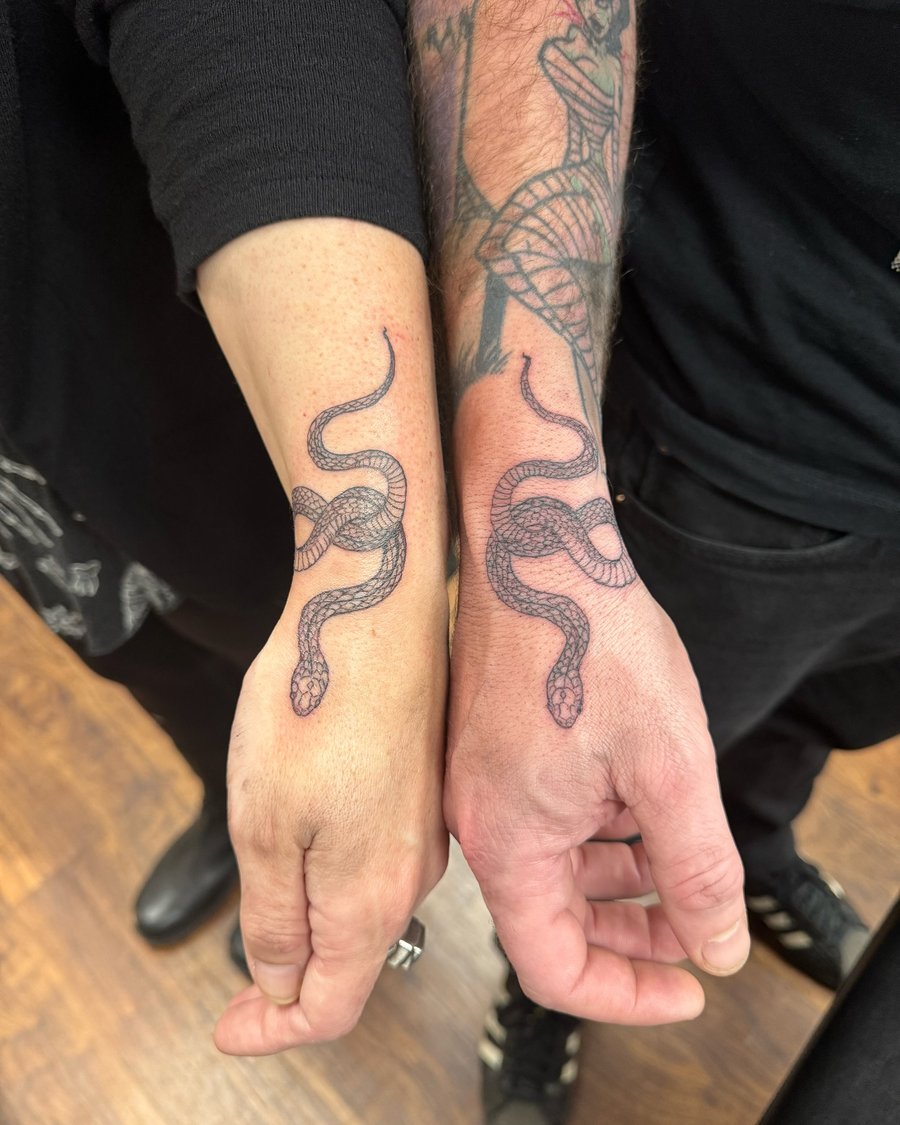 Matching blackwork snake tattoos on the hands with detailed linework and a graphic style — by Sandra Price, los angeles