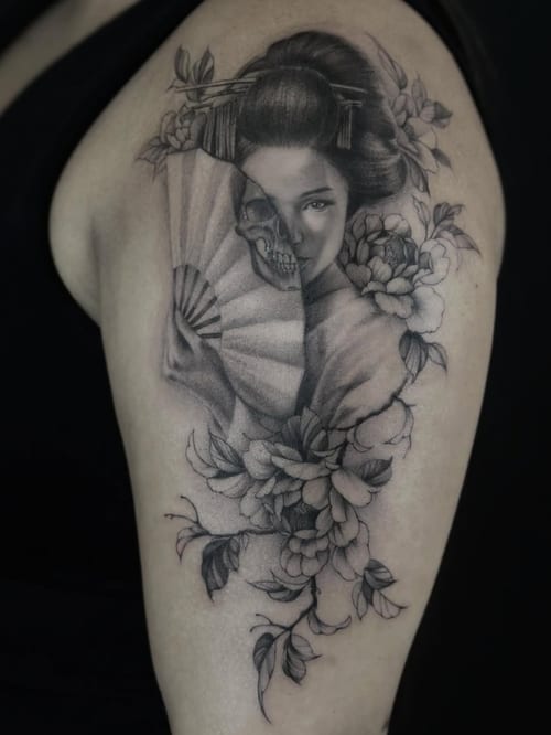 A black and grey tattoo on the upper arm depicting a woman with a fan and a skull, surrounded by flowers, in a realistic and Japanese style — by Jian Liang, los angeles