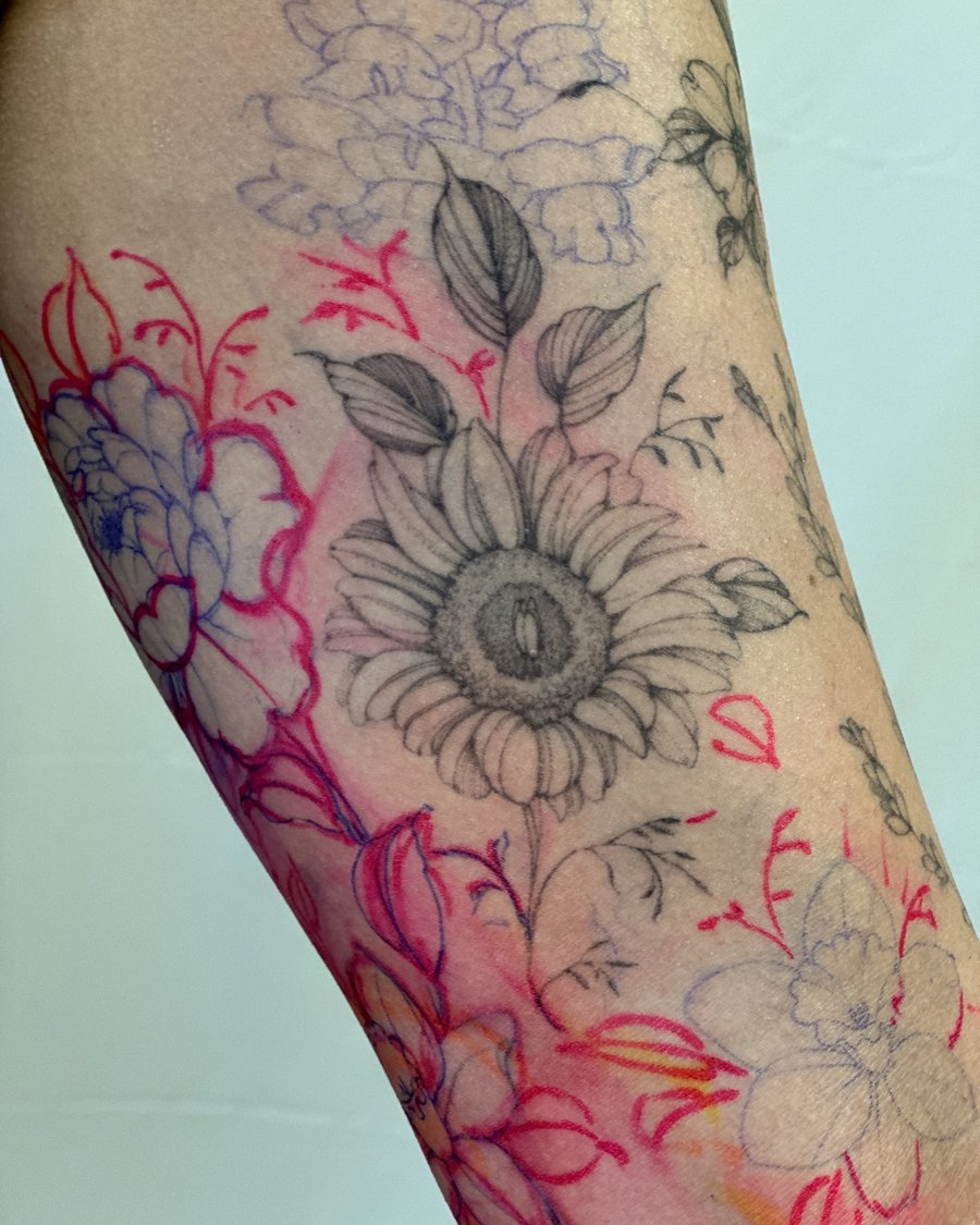 A delicate black and grey sunflower and floral design on the forearm with hints of color outlining — by Melanie Benoit, los angeles
