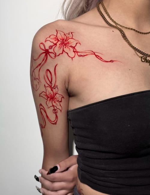 A fine line floral tattoo in red ink on the shoulder, featuring delicate flowers and flowing lines — by Shelby Bianco, los angeles
