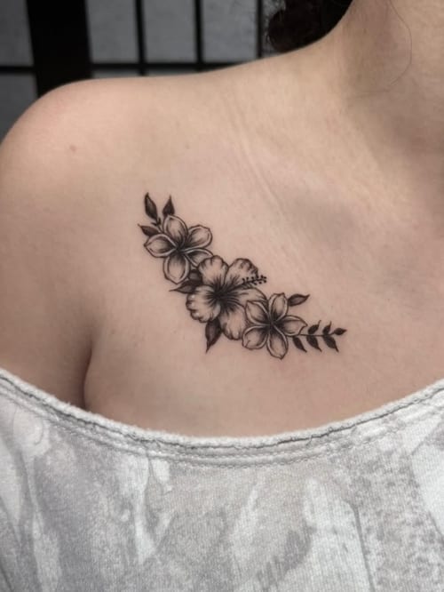 A delicate black and grey fine line floral tattoo on the collarbone, featuring hibiscus and other flowers with leaves — by Shelby Bianco, los angeles