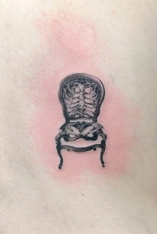 A black and grey surreal tattoo of a chair with a skeleton integrated into its design, featuring detailed linework — by Level tattoo, los angeles