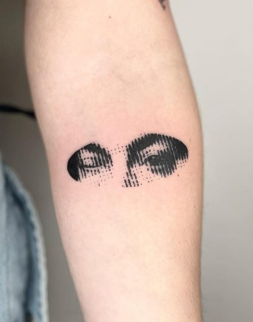 An abstract blackwork tattoo of a pair of eyes on the arm, featuring bold black lines and dotwork for shading — by Level tattoo, los angeles