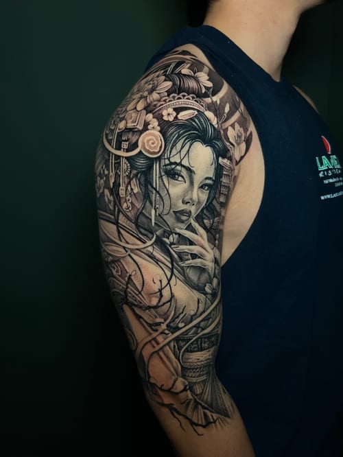 A detailed black and grey realism tattoo of a woman with floral elements on the upper arm, featuring intricate shading and Japanese influences — by imindisoul, los angeles