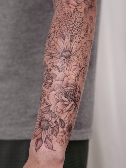 A delicate black and grey floral arrangement tattoo on the forearm featuring various flowers with intricate details — by Melanie Benoit, los angeles