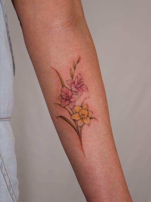 A delicate color flower bouquet tattoo on the forearm, featuring fine line work and a botanical style — by Melanie Benoit, los angeles