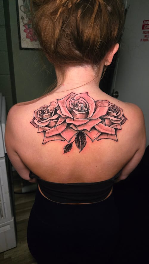 A black and grey tattoo of three roses on the upper back, featuring fine line work and detailed shading — by Dretty, los angeles
