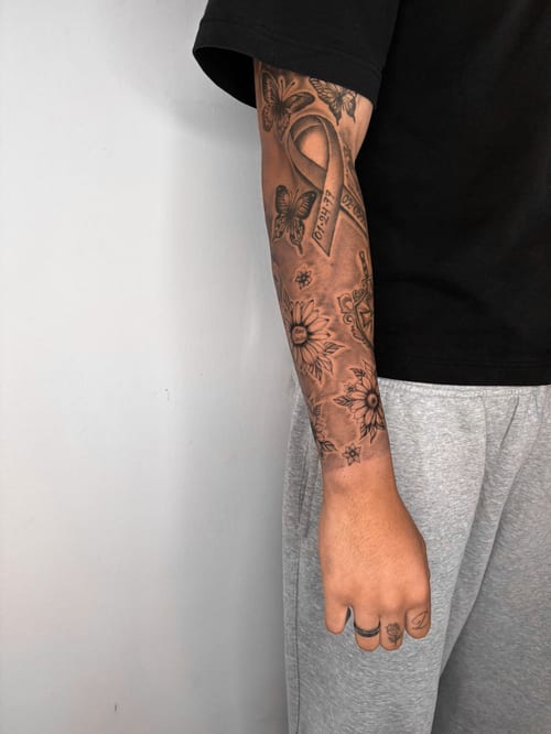 A black and grey tattoo on the forearm featuring butterflies, flowers, and a ribbon with fine line details — by Edgar Armas Rodriguez, los angeles