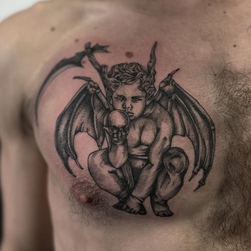 A black and grey tattoo of a cherub with wings holding a skull on the chest, featuring dotwork shading — by Maddie Ramirez, los angeles