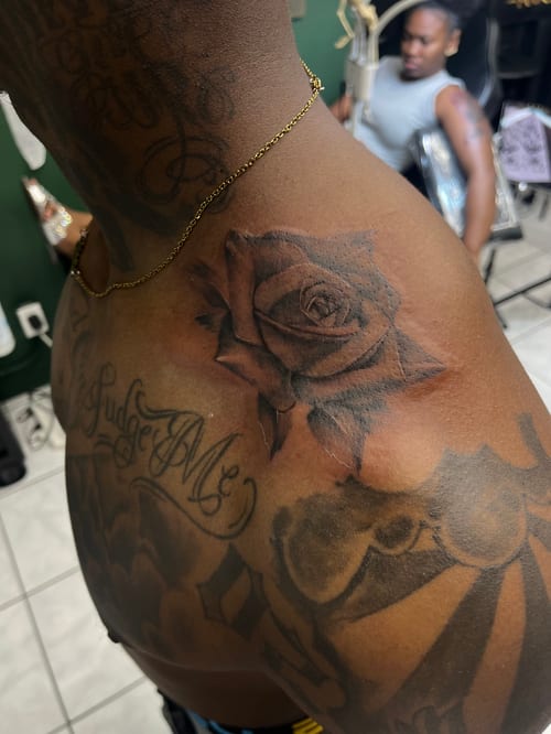 A black and grey realism tattoo of a rose with script on the shoulder, featuring detailed shading and lettering — by Mr._Folks, los angeles