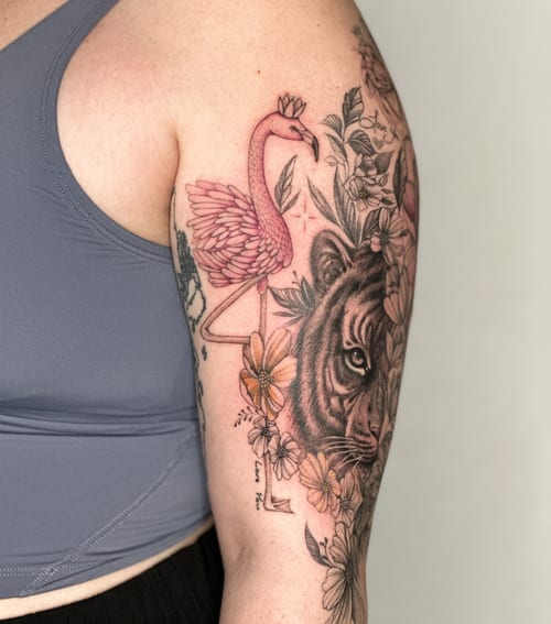 A colorful tattoo of a flamingo and tiger surrounded by flowers on the upper arm, blending illustrative and realistic styles — by Melanie Benoit, los angeles