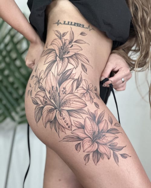 A delicate black and grey tattoo of lily flowers on the hip with intricate floral details — by Melanie Benoit, los angeles