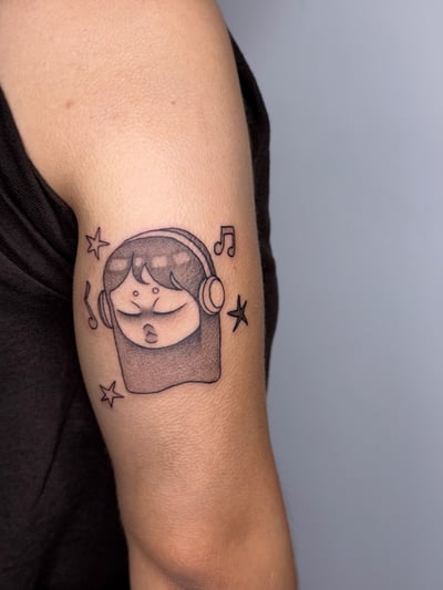 A minimalist black and grey tattoo of a cartoon face wearing headphones, surrounded by musical notes and stars, located on the upper arm — by lunayflorestattoo, los angeles
