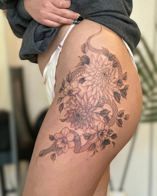 A delicate black and grey tattoo of a snake intertwined with flowers on the thigh, featuring fine line work and intricate details — by Melanie Benoit, los angeles