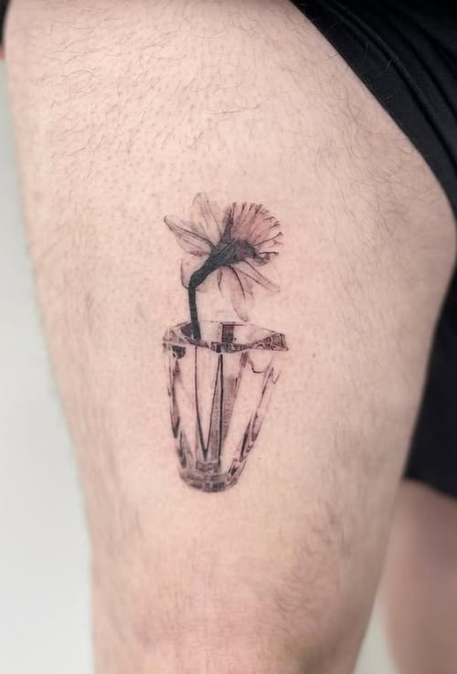 A fine line black and grey tattoo of a flower in a vase on the thigh, featuring delicate linework and minimal shading — by Level tattoo, los angeles