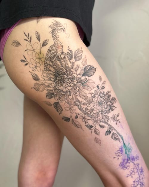 A black and grey dragon intertwined with flowers on the thigh, featuring delicate and ornate Japanese style elements — by Melanie Benoit, los angeles