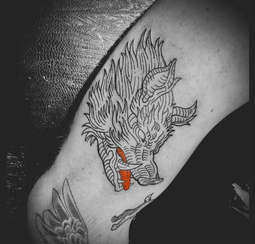 A linework tattoo of a wolf's head on the upper arm, primarily in black ink with striking red accents on the eyes and tongue — by Tag Devilish, los angeles
