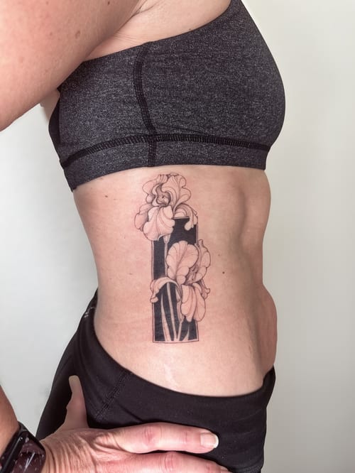 A delicate black and grey fine line flower tattoo on the rib, featuring a minimalist design with blackwork elements — by Melanie Benoit, los angeles