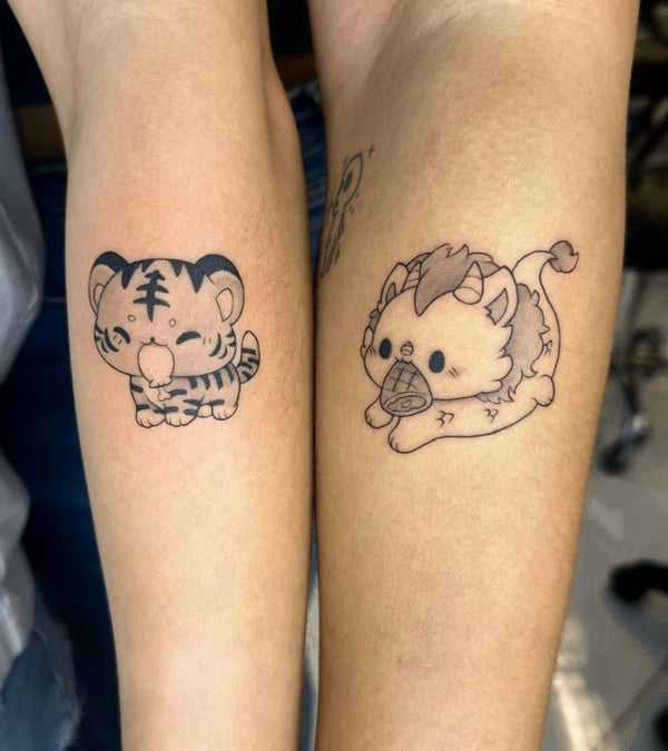 Two small, cute black and grey tattoos on the forearm featuring a cartoon-style tiger and lion with minimalistic details — by otaybeatdown, orange, ca