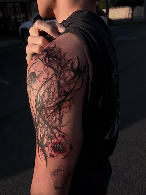 An abstract black and red floral and thorn design on the upper arm, featuring bold blackwork and graphic elements — by Hannah , fountain valley, ca