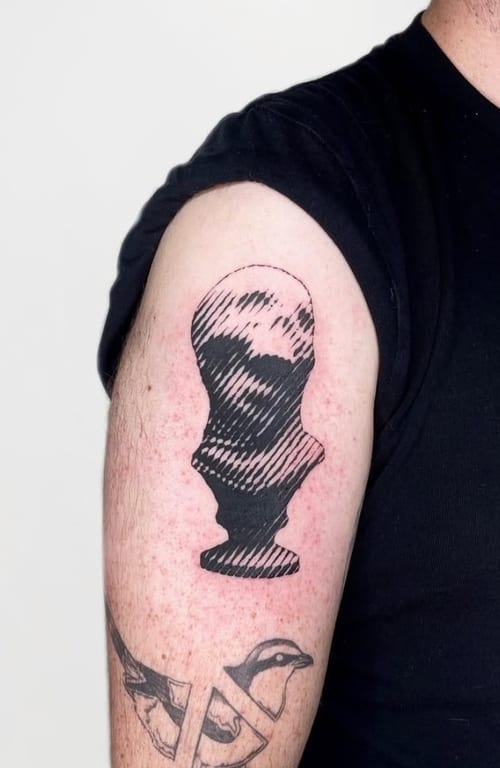 An abstract black and grey linework portrait on the upper arm, featuring a stylized bust with a striped pattern — by Level tattoo, los angeles