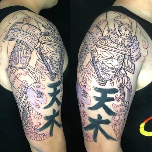 A bold black and grey samurai tattoo on the upper arm with Japanese script, featuring intricate armor details — by Sandra Price, los angeles