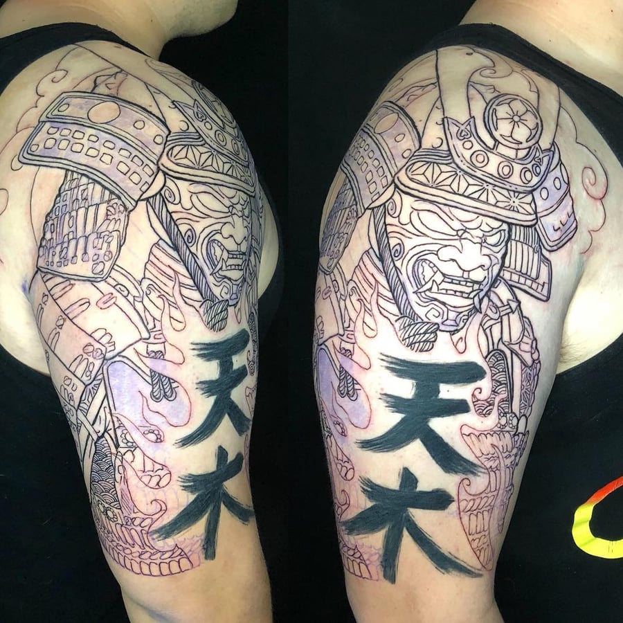 A bold black and grey samurai tattoo on the upper arm with Japanese script, featuring intricate armor details — by Sandra Price, los angeles