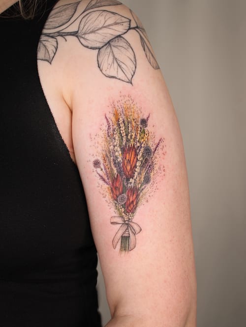 A colorful bouquet of flowers tattooed on the upper arm with fine line and delicate details — by Melanie Benoit, los angeles