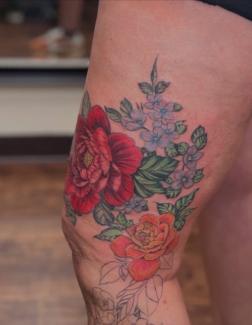 A colorful floral bouquet tattoo on the thigh featuring roses and other flowers in a realistic style — by Sandra Price, los angeles