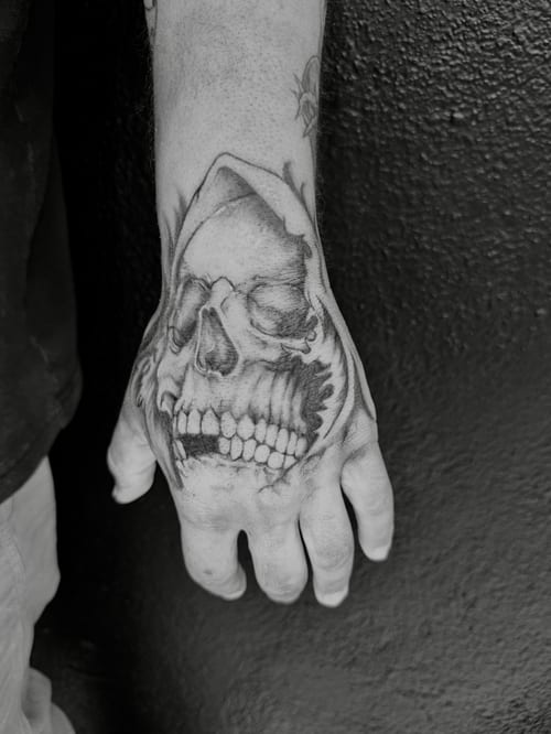 A bold black and grey skull tattoo on the hand with realistic shading and detail — by Kiera Garvin, los angeles