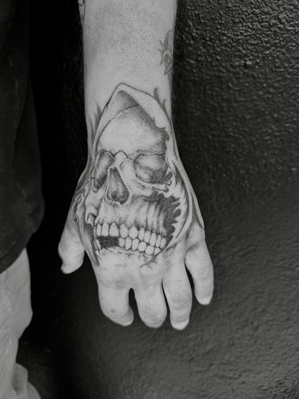 A bold black and grey skull tattoo on the hand with realistic shading and detail — by Kiera Garvin, los angeles