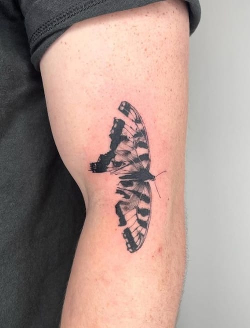 A black and grey realistic butterfly tattoo on the upper arm with detailed wing patterns — by Level tattoo, los angeles