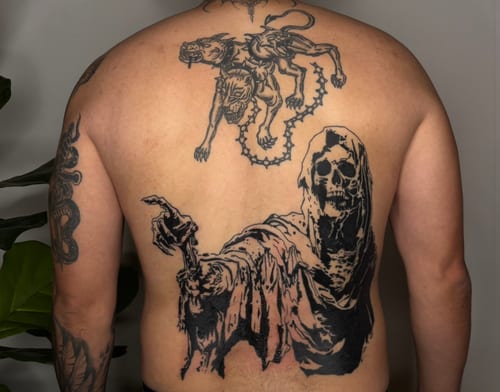 A large blackwork tattoo covering the full back, featuring a skeleton in a cloak pointing forward and a stylized animal above, both in dark, bold lines — by velvet devil, los angeles