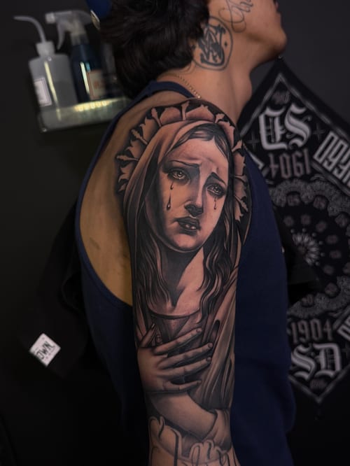 A realistic black and grey portrait of a weeping woman with religious iconography, covering the full sleeve — by Eddie Rodriguez, los angeles