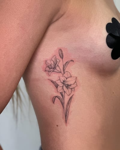 A delicate black and grey fine line tattoo of lily flowers on the rib, featuring minimalistic floral design — by Melanie Benoit, los angeles