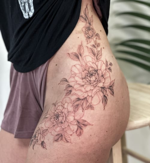 A delicate black and grey floral arrangement tattoo on the hip, featuring fine line work and soft shading — by Melanie Benoit, los angeles