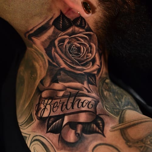A bold black and grey tattoo featuring a realistic rose and script lettering on the neck — by Johnny Ayala, los angeles